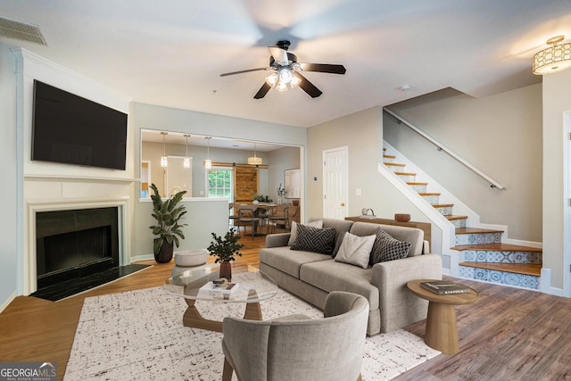 living room with visible vents, a fireplace with flush hearth, ceiling fan, wood finished floors, and stairs