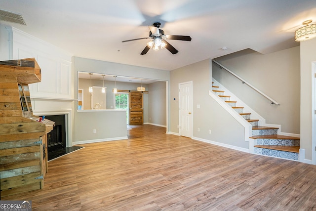 unfurnished living room featuring light wood finished floors, stairs, visible vents, and a fireplace