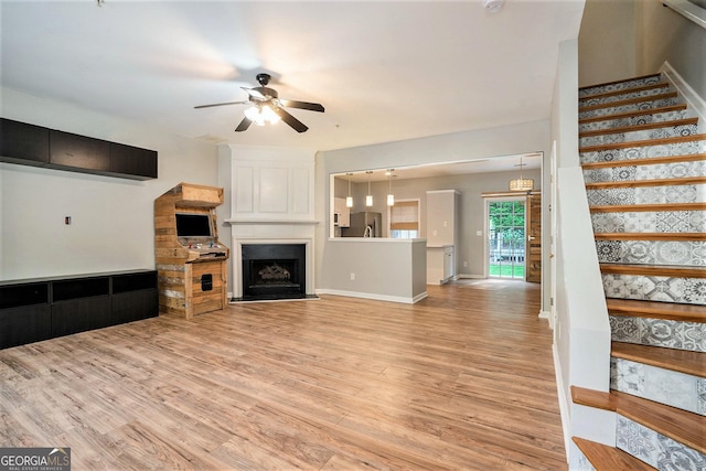 living room with baseboards, ceiling fan, stairway, light wood-style floors, and a fireplace