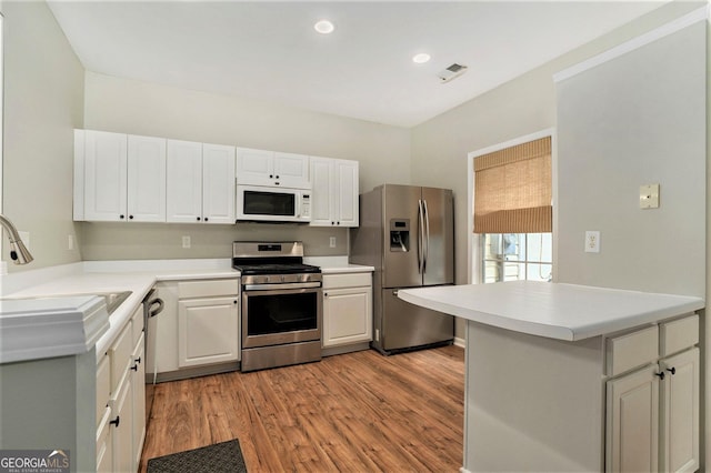 kitchen featuring a peninsula, white cabinetry, light countertops, appliances with stainless steel finishes, and light wood finished floors