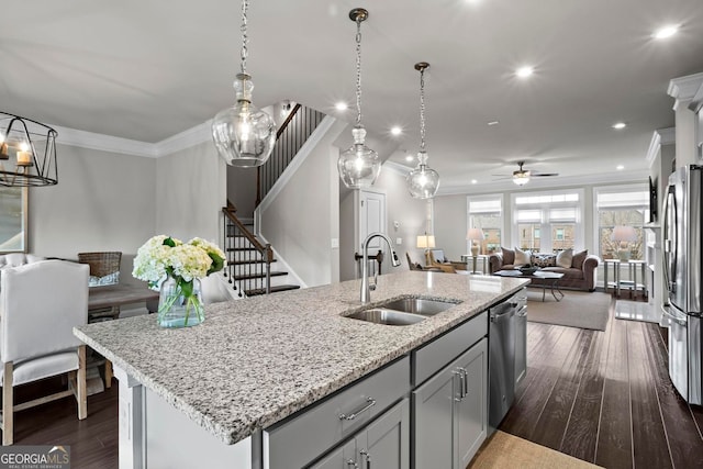 kitchen featuring dark wood finished floors, appliances with stainless steel finishes, open floor plan, crown molding, and a sink