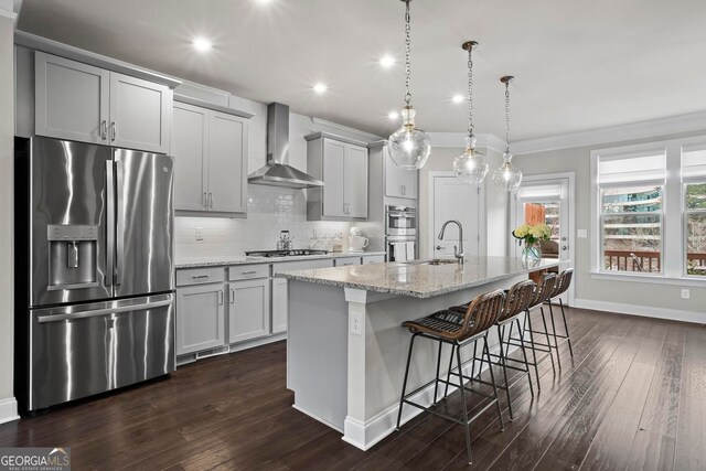 kitchen featuring decorative backsplash, an island with sink, wall chimney exhaust hood, stainless steel appliances, and a sink