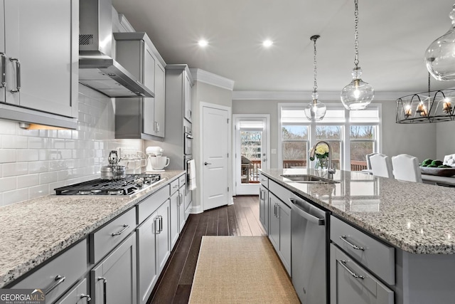 kitchen with crown molding, stainless steel appliances, gray cabinetry, a sink, and wall chimney range hood