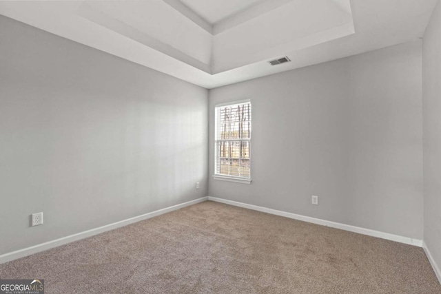 carpeted empty room featuring baseboards, visible vents, and a tray ceiling