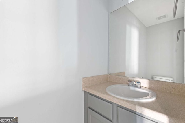 bathroom featuring toilet, vanity, and visible vents