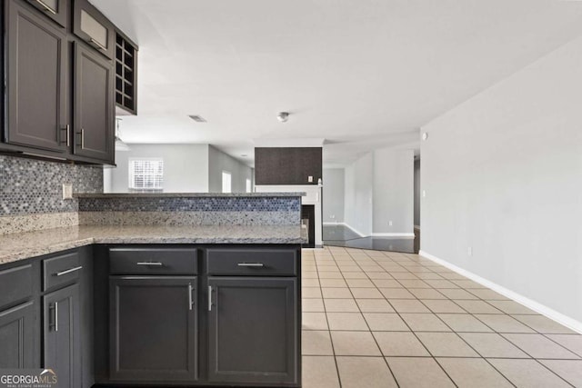 kitchen featuring light tile patterned floors, a peninsula, baseboards, backsplash, and light stone countertops