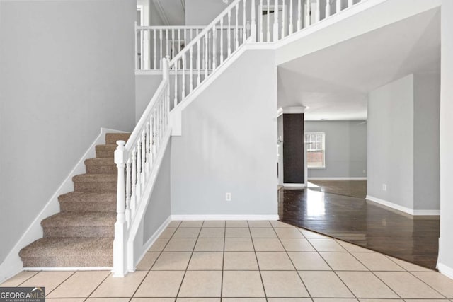 stairs featuring a towering ceiling, tile patterned flooring, and baseboards