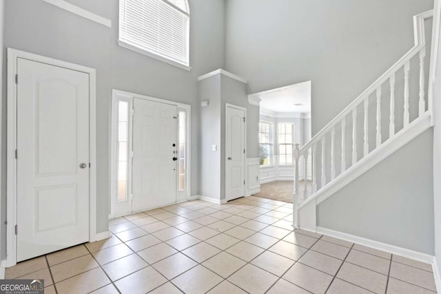 entryway featuring light tile patterned floors, baseboards, a towering ceiling, stairway, and ornamental molding