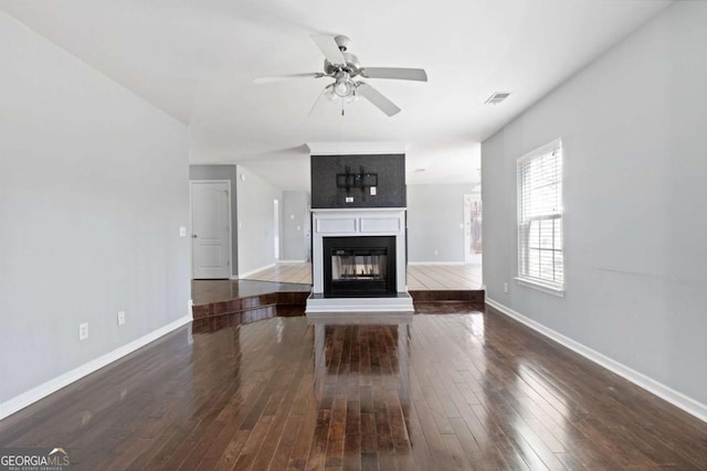 unfurnished living room featuring a glass covered fireplace, visible vents, baseboards, and hardwood / wood-style flooring