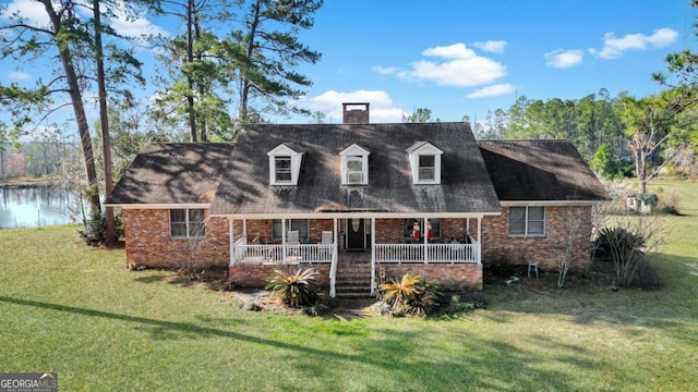 new england style home with a porch, a front yard, brick siding, and a water view