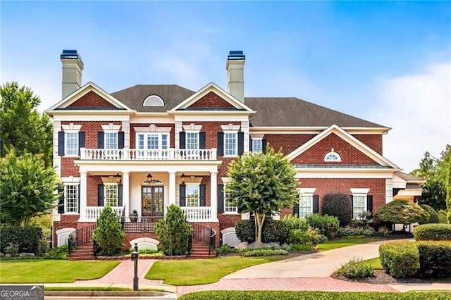 view of front of house featuring a balcony, covered porch, a chimney, and brick siding