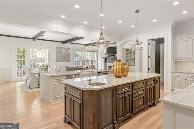 kitchen with light wood-style flooring, a sink, a large island with sink, and a healthy amount of sunlight