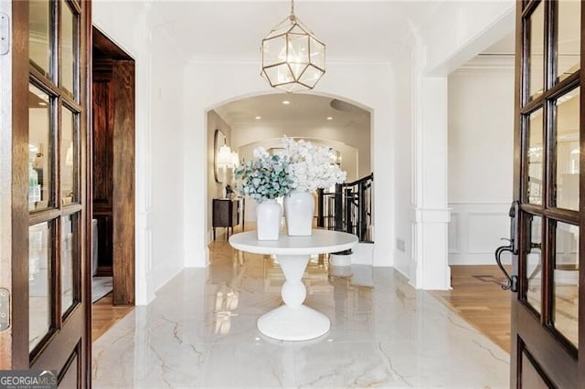 interior space featuring crown molding, marble finish floor, a notable chandelier, and a decorative wall