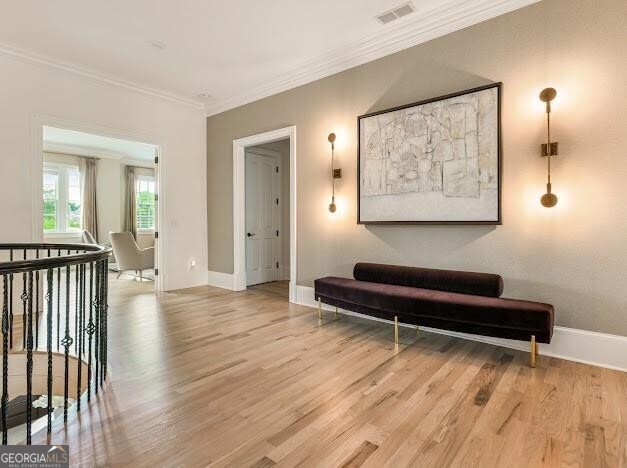 interior space featuring light wood-type flooring, visible vents, crown molding, and baseboards