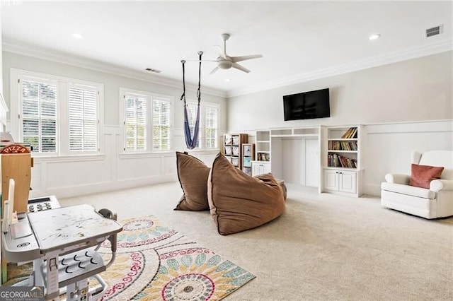 carpeted living area with visible vents, ornamental molding, a ceiling fan, and wainscoting