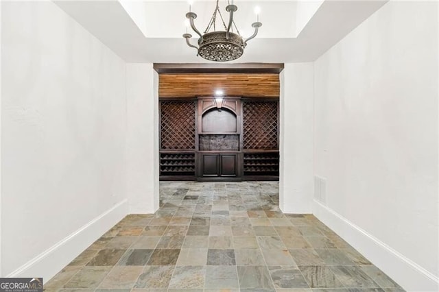 wine room featuring a chandelier, a tray ceiling, stone finish floor, and baseboards