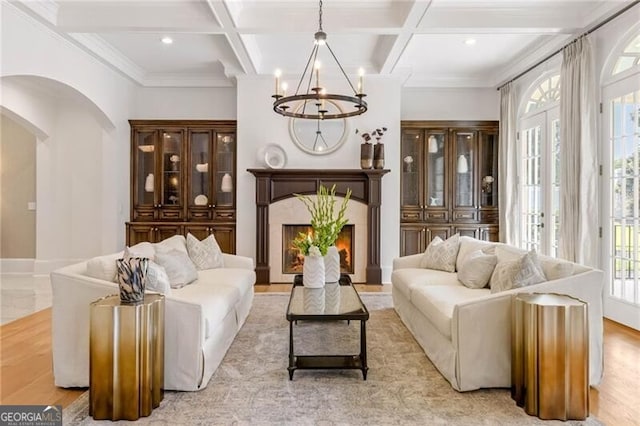 sitting room with coffered ceiling, a high end fireplace, beam ceiling, an inviting chandelier, and crown molding