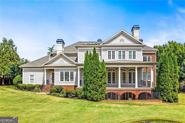 back of property featuring brick siding, a yard, a chimney, and a balcony