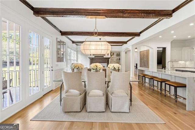 dining room featuring arched walkways, a wealth of natural light, beam ceiling, and light wood-style floors