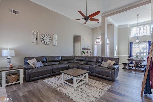 living room with a towering ceiling, visible vents, wood finished floors, and ornamental molding