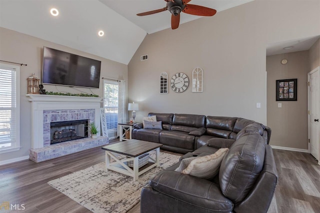 living area with a brick fireplace, baseboards, visible vents, and wood finished floors