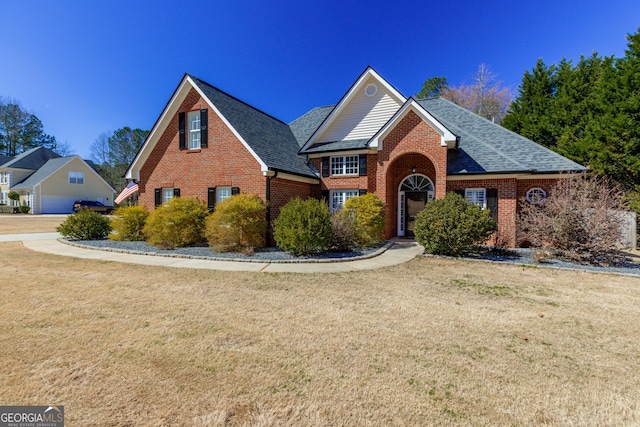 traditional-style home with a shingled roof, brick siding, and a front lawn