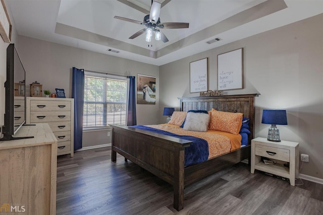 bedroom featuring baseboards, visible vents, a tray ceiling, and wood finished floors