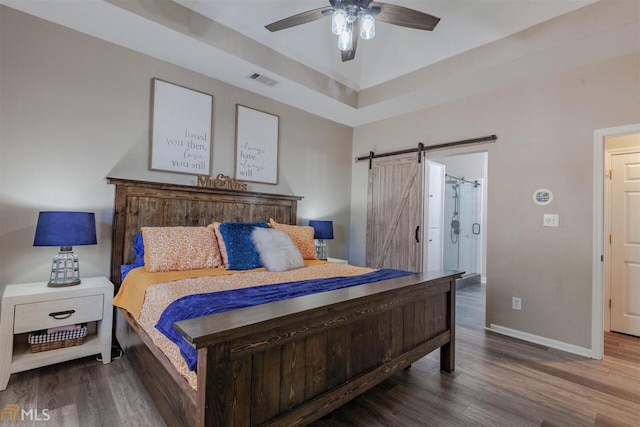 bedroom with visible vents, a barn door, ceiling fan, wood finished floors, and baseboards