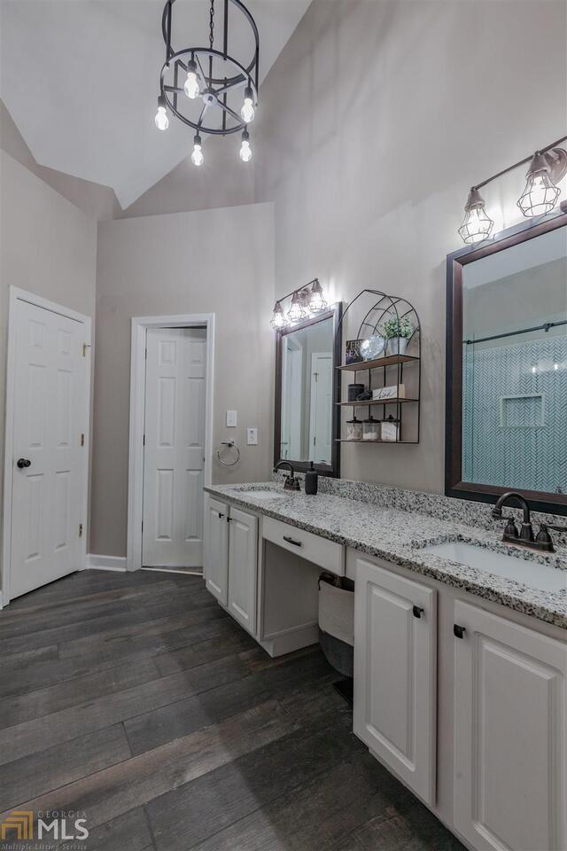 bathroom with double vanity, high vaulted ceiling, wood finished floors, and a sink