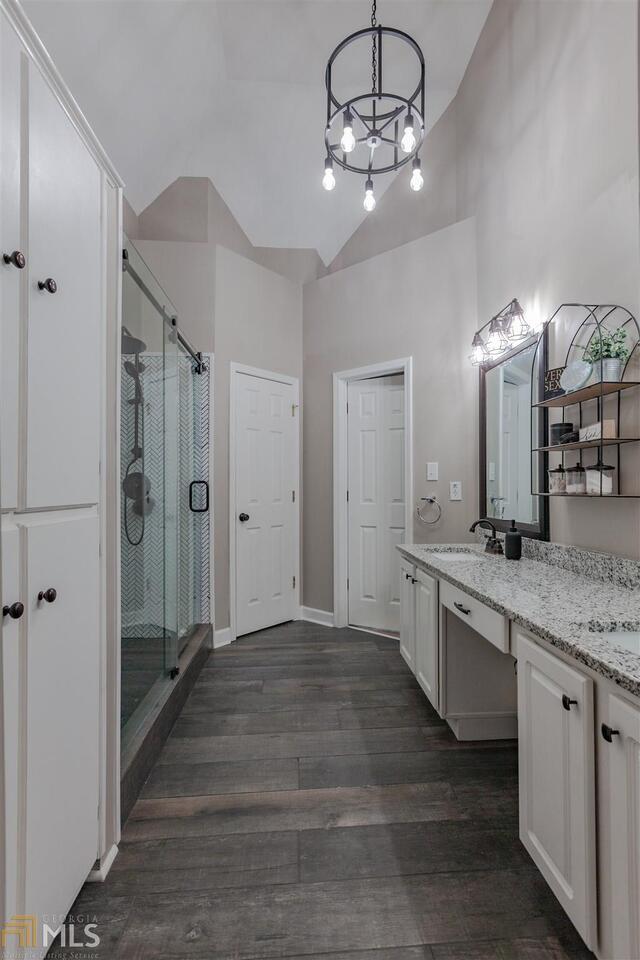 bathroom featuring a chandelier, wood finished floors, vanity, baseboards, and a shower stall