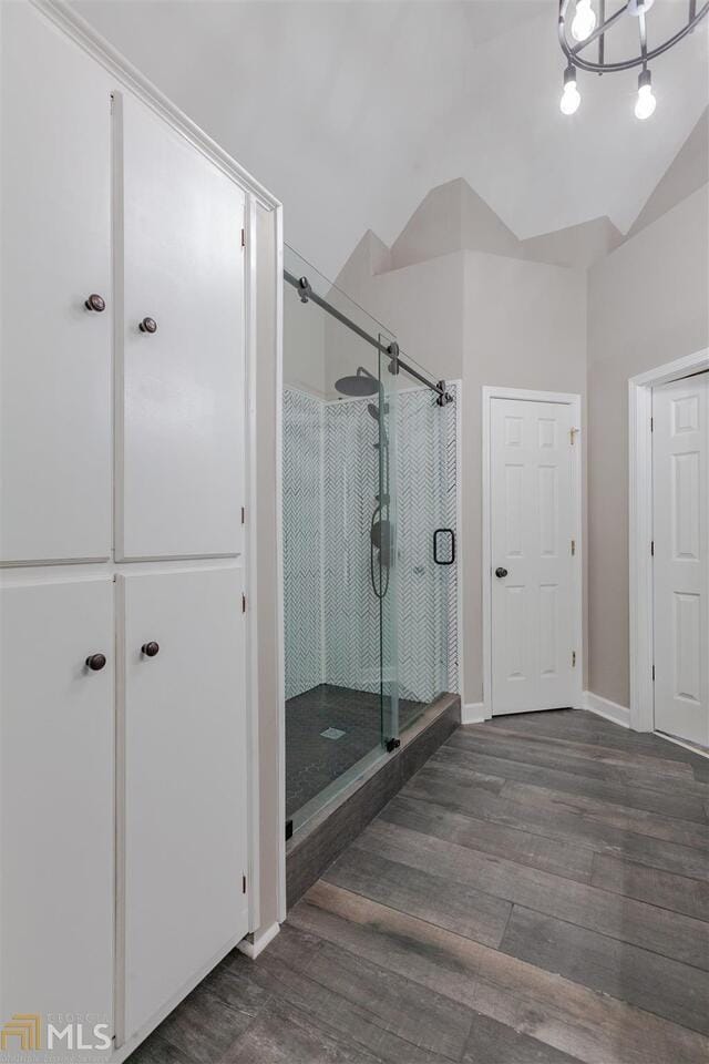 full bath with a stall shower, vaulted ceiling, baseboards, and wood finished floors