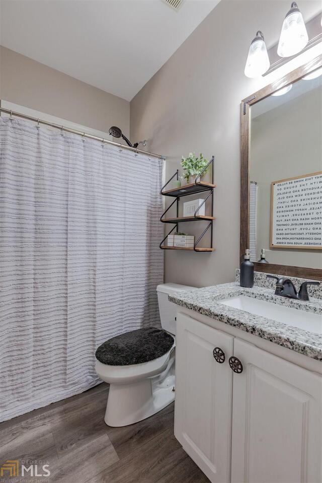 full bath featuring toilet, curtained shower, wood finished floors, and vanity