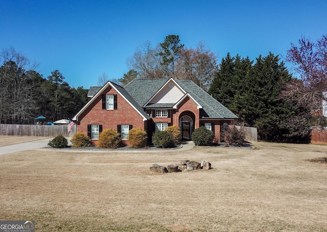 traditional-style house featuring brick siding, fence, a front lawn, and roof with shingles