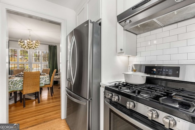 kitchen with a notable chandelier, backsplash, appliances with stainless steel finishes, light wood-style floors, and under cabinet range hood