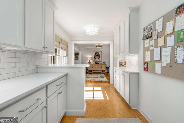 kitchen with light wood-style flooring, white cabinetry, baseboards, light countertops, and decorative backsplash