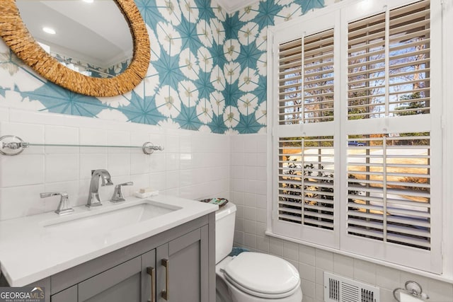 bathroom featuring tile walls, visible vents, toilet, vanity, and wallpapered walls