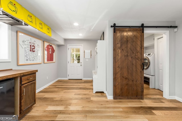 foyer with washer / clothes dryer, baseboards, light wood finished floors, and a barn door