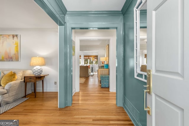 corridor featuring ornamental molding, light wood-style floors, and baseboards