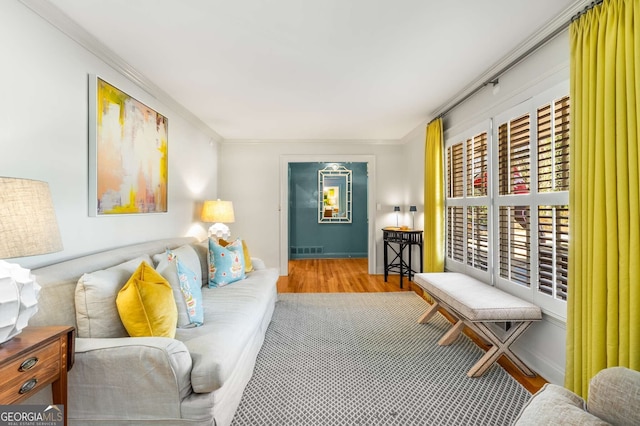 living room featuring baseboards, crown molding, visible vents, and wood finished floors