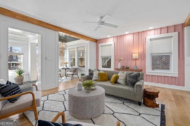 living area with light wood-type flooring, beam ceiling, recessed lighting, and ceiling fan with notable chandelier