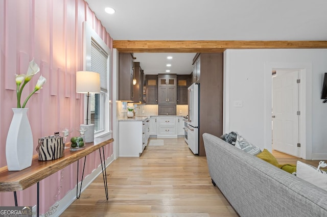 kitchen featuring light wood-style flooring, light countertops, high end fridge, beam ceiling, and glass insert cabinets