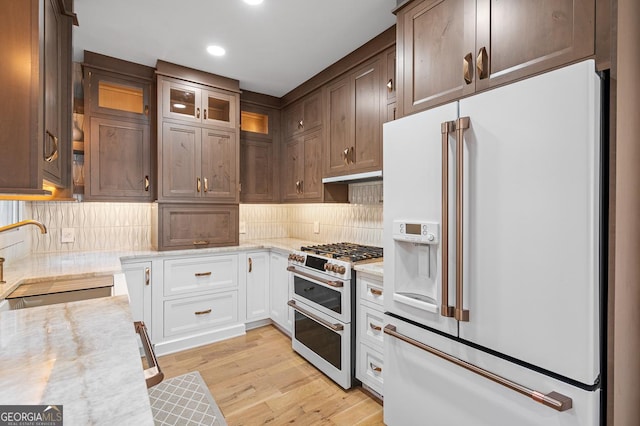 kitchen featuring backsplash, a sink, light stone countertops, light wood-type flooring, and white appliances