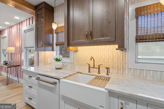 kitchen with backsplash, light stone countertops, white dishwasher, light wood-style floors, and a sink