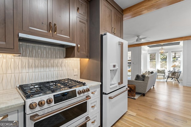 kitchen featuring range with two ovens, high end white fridge, decorative backsplash, light wood-type flooring, and under cabinet range hood