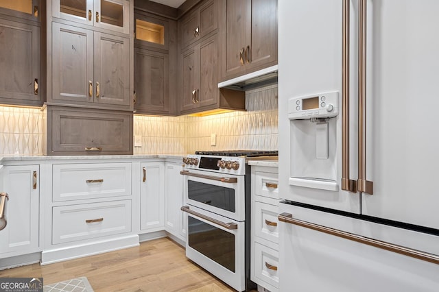 kitchen featuring white appliances, glass insert cabinets, under cabinet range hood, white cabinetry, and backsplash