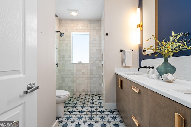 bathroom featuring double vanity, tiled shower, a sink, and toilet