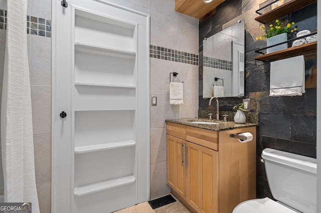 bathroom featuring toilet, vanity, and tile walls