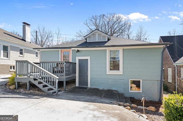 back of house featuring concrete driveway, roof with shingles, and a deck