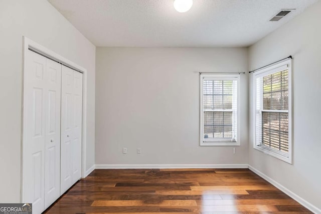 unfurnished bedroom featuring visible vents, a textured ceiling, baseboards, and wood finished floors