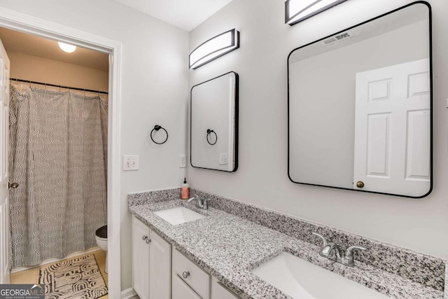 full bathroom with toilet, double vanity, visible vents, and a sink